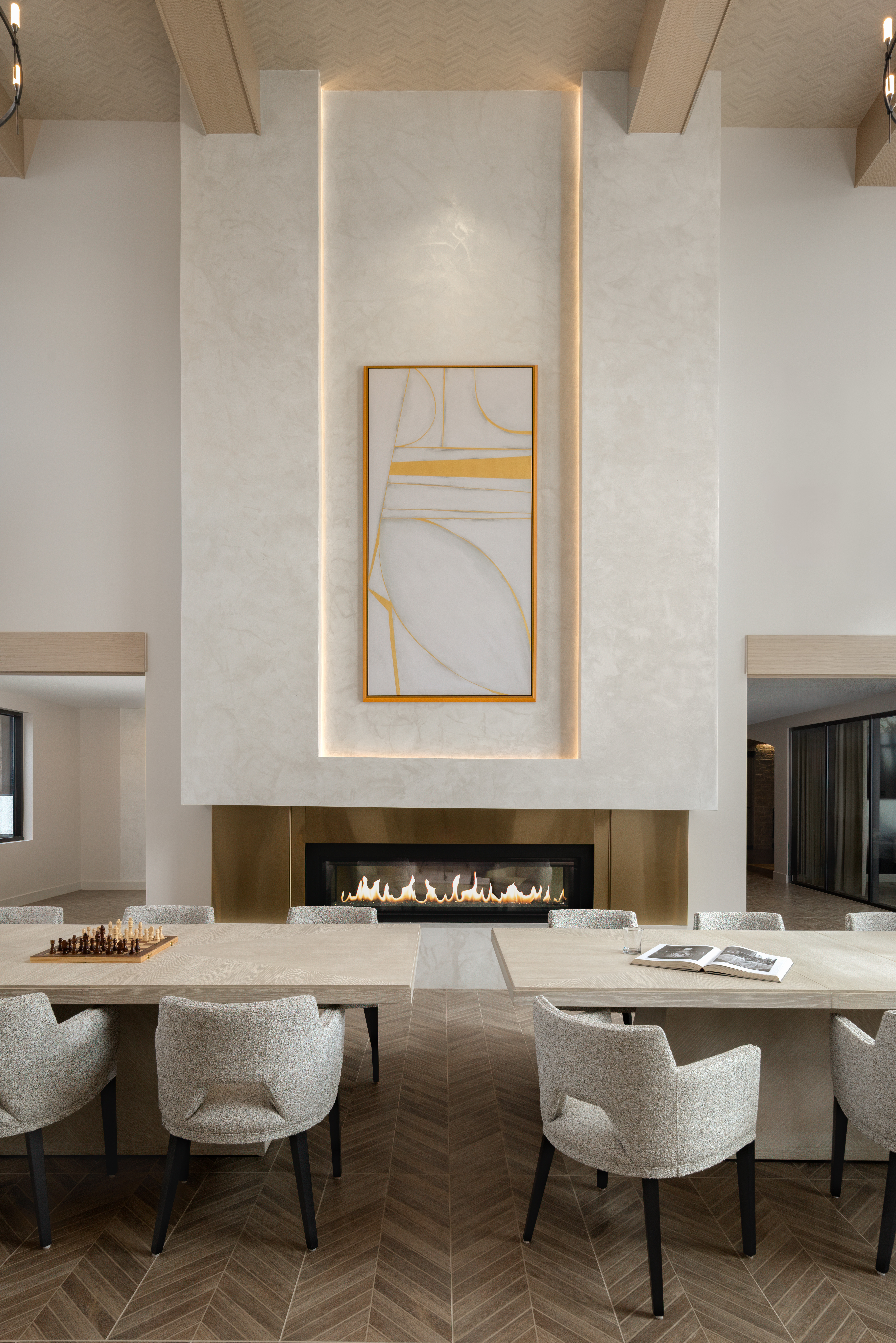 Luxury kitchen and fireplace amenity featuring communal dining table, upholstered seating, architectural fireplace surround, and high-end interior design for multifamily communities.