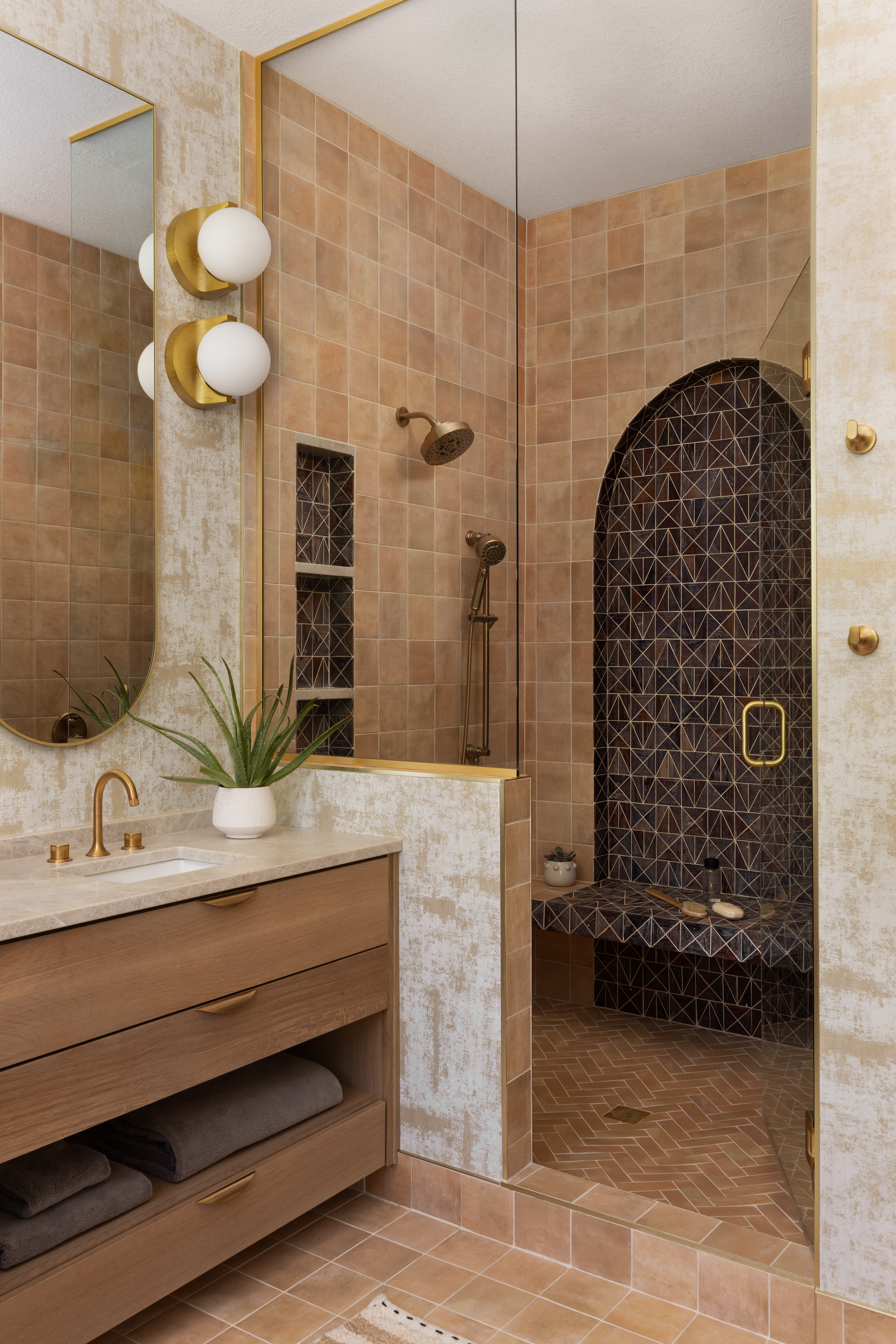 Luxury bathroom featuring custom tile shower with arched opening, integrated bench, brass fixtures, and refined interior design details.