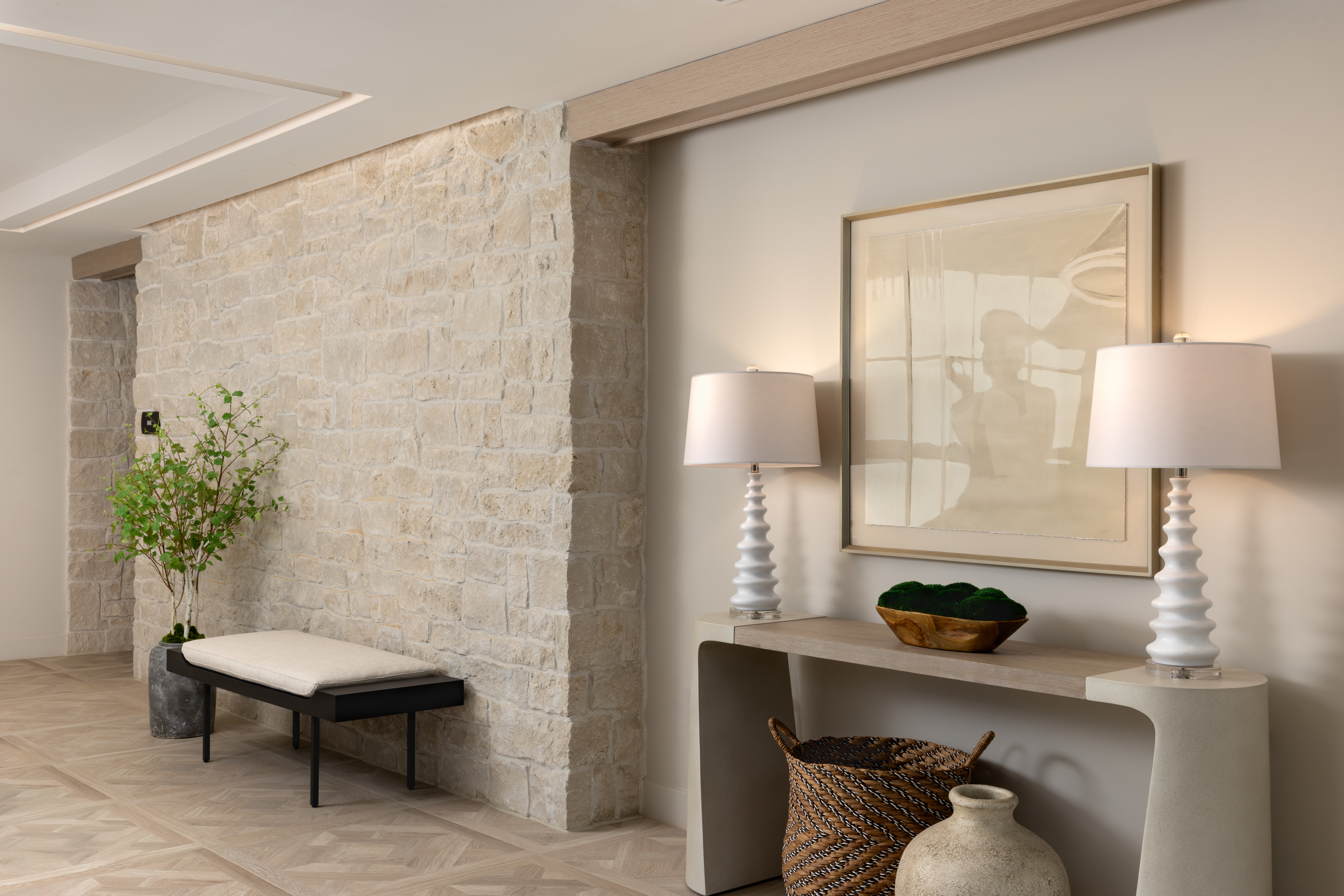 Luxury commercial entryway with stone feature wall, custom bench seating, curated artwork, and hospitality-inspired interior design for multifamily communities.