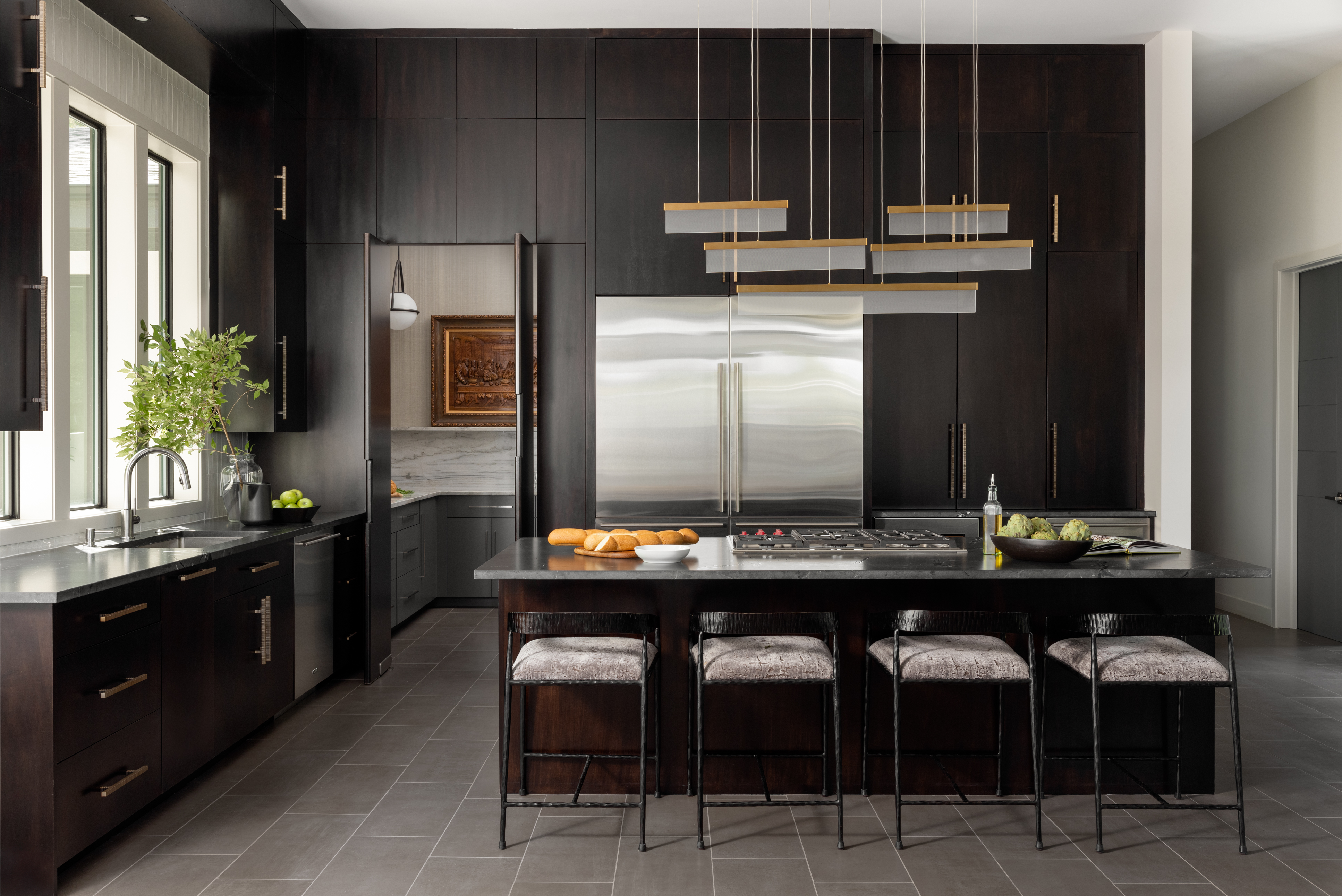 Luxury residential kitchen seating area featuring custom island stools, dark wood cabinetry, integrated appliances, and modern interior design.